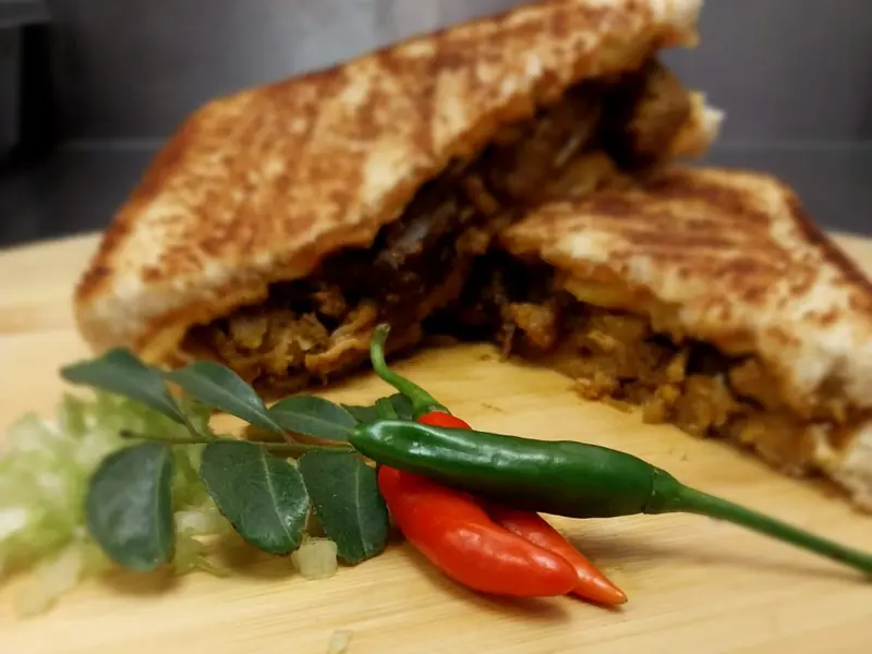 Toasted mutton curry sandwich cut in half, with fresh chillies and curry leaves